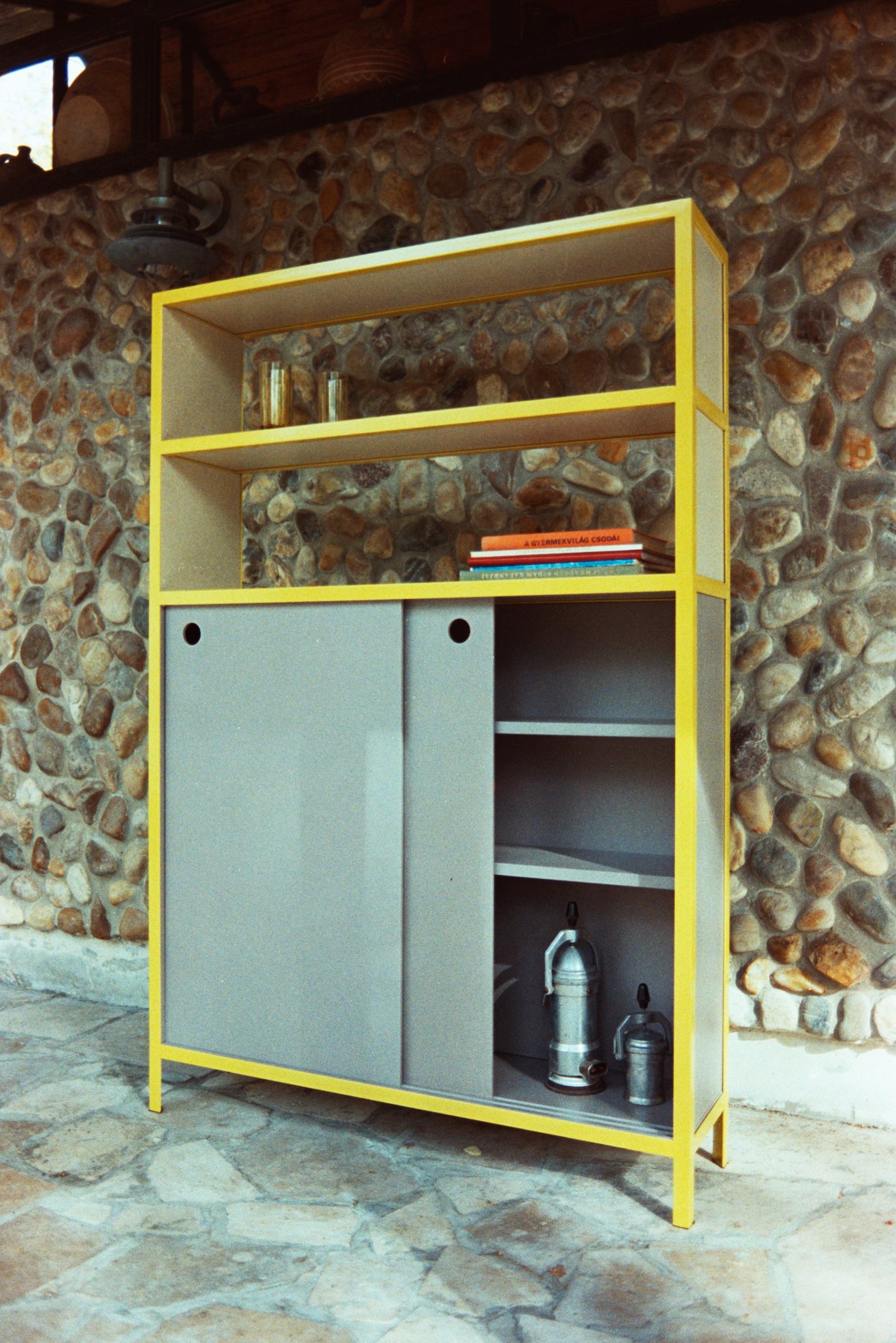 Frame Shelf with a yellow steel frame against a stone wall
